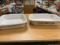 Two large white casserole dishes on a wooden surface, one plain and one with vegetable pattern on the side.