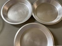 Three round metal pie plates arranged closely on a flat surface showing surface scratches and consistent use wear.