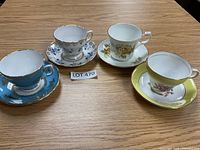 Four bone china tea cup and saucer sets arranged on a wooden table.