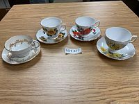 Four bone china cups with matching saucers on a wooden table, various floral designs and gold trim visible.