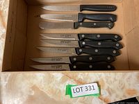 Photo showing a set of 11 knives including 5 serrated black-handled steak knives, and other knives in a cardboard box.