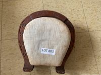 Top view of antique foot stool showing hand-carved wood with 'GOOD LUCK' inscription and fabric cushion with signs of wear.