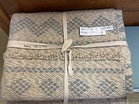 Folded woven area carpet tied with cotton strap, showing general pattern and texture