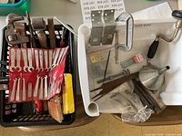 Overview of the assorted hand tools including pipe wrenches, fabric pouch with wrenches, hand drill, funnel, clamps, and metal tools.