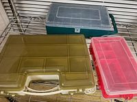 Three rectangular plastic storage containers with clear lids and handles in green, tan, and red colors displayed on metal shelving unit.