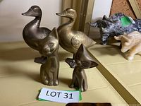 Four brass animal figurines displayed together: two cats and two waterfowl, placed on a beige surface with a lot label.