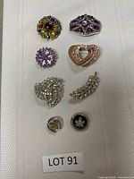 Eight brooches laid out on a white surface showing overall condition and designs.