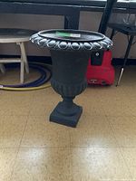 Front view of the black cast iron outdoor planter showing the entire urn on the floor, with decorative rounded rim and fluted body.