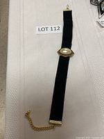 Black velvet choker with central faux pearl and gold-tone metal decoration laid flat on surface with Lot 112 label