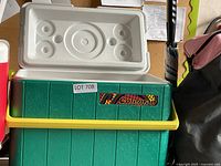 Closed green Coleman cooler with yellow handle and white lid with cup holders shown from the side.
