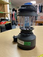 Full view of black Coleman lantern showing clear glass globe and power cord wrapped at base.