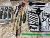 Wide view of cutlery tray with spoons, forks, knives organized and cooking utensils spread out on table.