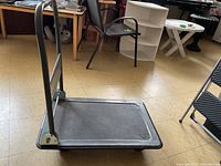 Gray Hurricane platform cart dolly with textured surface and metal folding handle photographed in a room with chairs and tables.