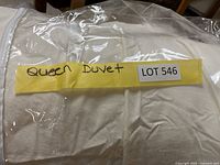 Duvet folded, rolled, and stored inside clear plastic zippered bag with yellow label stating Queen Duvet LOT 546.
