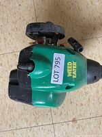 Close up photo of the green Weed Eater gas engine with LOT 795 sticker attached, showing the brand name clearly.