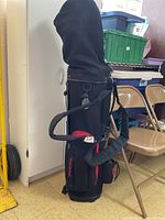 Photo of full black and red TrailPak golf bag standing with adjustable padded shoulder strap and club cover attached.