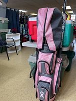 Full view of pink and gray golf bag with visible zippered compartments and shoulder strap.