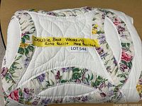Folded view of the quilt showing the floral print fabric and white quilting, with a yellow label stating: 'Double Bed Wedding Ring Quilt Hand Quilted'.