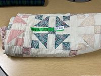 Folded hand made quilt with visible label showing measurements 84x92 inches along with dealer lot number. Quilt shows patchwork in multiple fabric patterns and colors.