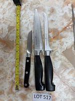 All three Henckels cutting knives laid flat on marble countertop with measuring tape for scale, showing full blades and handles.