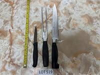 Three Henckels cutting tools shown side-by-side on marbled surface: paring knife, carving fork, and chef's knife, with a measuring tape beside for size reference.