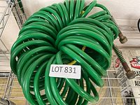 Green coiled garden hose on metal rack with label Lot 831