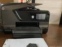 Side-front view of HP OfficeJet Pro 8600 printer showing paper tray open and touchscreen display.