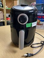 Front and side view of the black Kalorik air fryer showing the handle, power cord, and overall design.