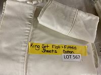 Folded king size flat and fitted sheets with pillowcases in cream or off-white cotton fabric, a handwritten note confirming fabric and set type is visible.