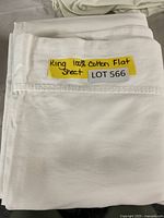Folded white king size flat sheet with label stating 'King 100% Cotton Flat Sheet' and lot number '566'.