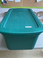 Full view of the large green plastic storage bin with lid, placed on a table.