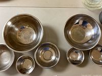 Set of seven metal mixing bowls arranged on a surface showing size variation and condition.