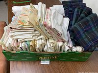 Large collection of pillowcases folded and neatly stacked in a green Pristine branded box, showing various floral and white pillowcases