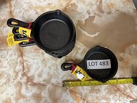 Stack of eight new mini cast iron fry pans with brand tags and measurement tape showing size around 4.5 inches