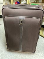 Front view of large brown fabric suitcase with single zipper and vertical logo band.