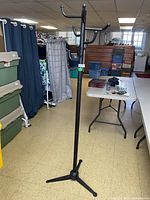 Full view of black metal coat rack stand in room with other furniture and storage bins in background.
