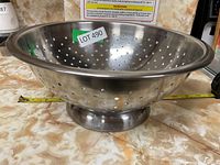 Angled view showing exterior, side handle, and pedestal base of metal colander on countertop.