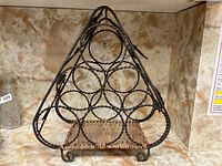 Front view of triangular metal wine rack with circular bottle holders and woven base, no decoration visible