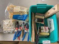 Photo showing brushes, roller covers, gloves, scraper tool and wooden sticks in teal container.