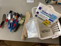 Overview of painting supplies including brushes, scraper, paint stir sticks, plastic bags, roller refills, and basket