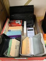 Lot of assorted office supplies including keyboard, calculator, pencil sharpener, paper, and organizer in a box