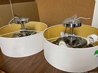 Pair of round ceiling light fixtures with white fabric shades and yellow interior lining, showing the fixtures side by side on a table.
