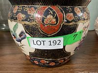 Close-up view of one planter showing floral emblem, bird, and gold detailing on black and cream background with the lot number sticker.