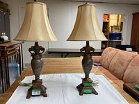 Pair of vintage-style table lamps with beige fabric bell-shaped shades and ornate metal bases on a wooden table.