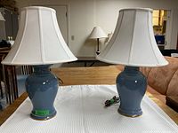Pair of matching table lamps with blue ceramic bases and white fabric shades on a white textured cloth.