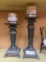 Both candle stands shown together, each topped with a wrapped pillar candle.