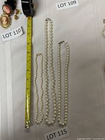 Three pearl necklaces displayed on a white surface with a measuring tape showing length of strands.