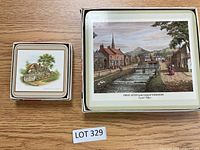 Two sets of Pimpernel coasters shown, smaller coasters stacked with cottage scenes, larger coasters in tin with scenic village print.