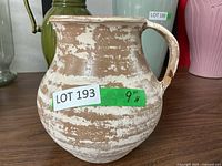 Front view of pitcher style planter showing distressed cream and tan finish, repaired handle, and chipped areas.