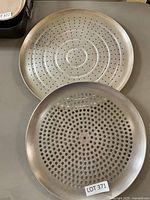 Two round metal pizza pans with perforations, one with large holes, one with small holes, both showing signs of use.